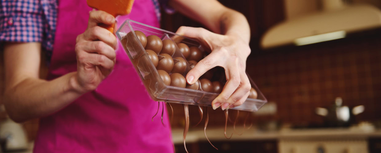 Mulher criando cascas de bombom na forma com chocolate.