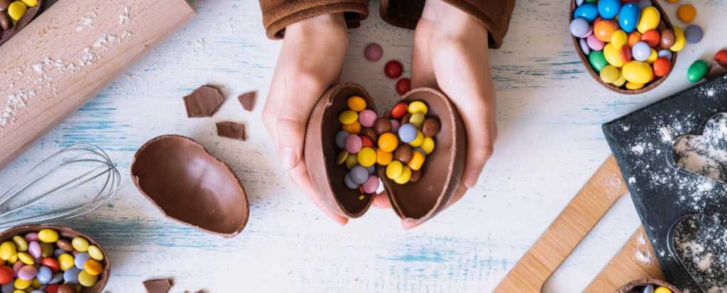 Mãos abrindo mini ovo de Páscoa recheado com disquetes de chocolate.