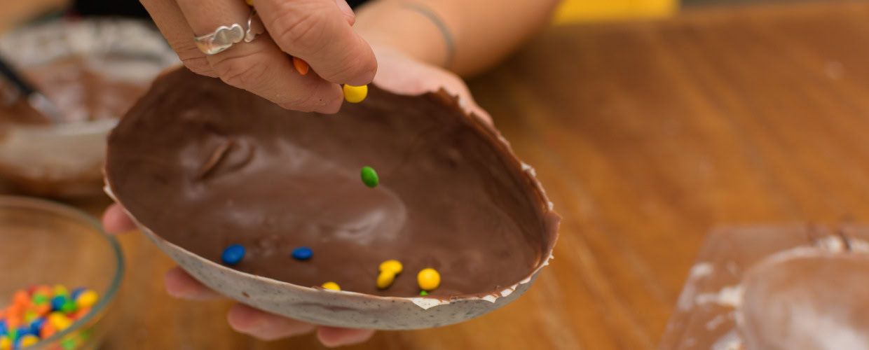 Pessoa colocando confete de chocolate colorido na casa do ovo de Páscoa.