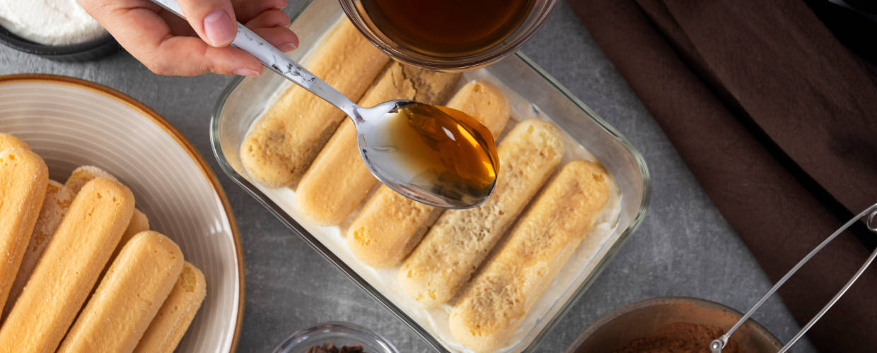 Café sendo despejado em colher para umedecer biscoito do pavê.