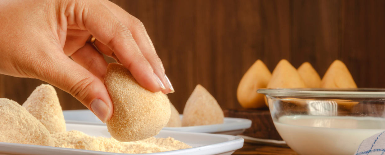Mão empanando coxinha.